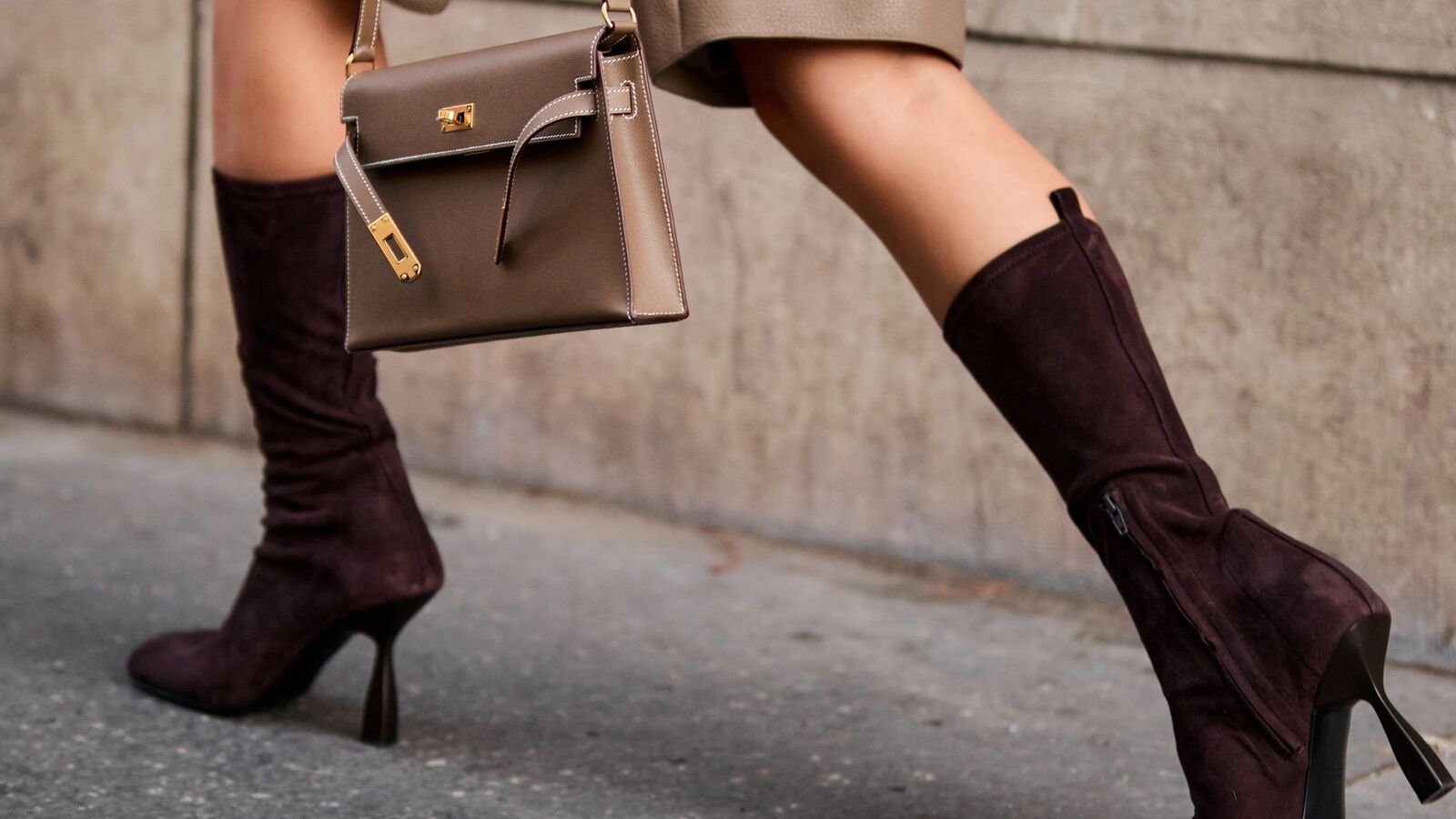 Woman wears trouser shorts and matching beige handbag and calf-hugging boots while walking