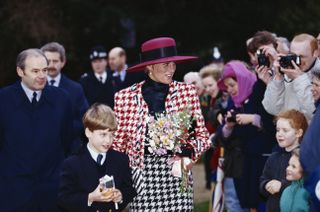 Princess Diana wearing a red, white and black checkered skirt suit and big red hat walking with Prince William as members of the public took her pictures