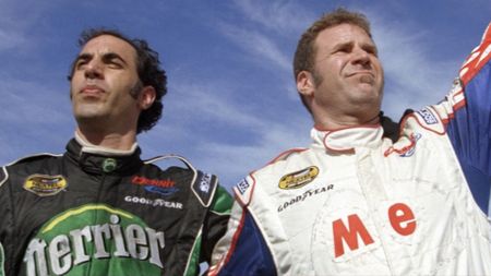 Jean Girard (Sacha Baron Cohen) and Ricky Bobby (Will Ferrell) wave to the crowd at the Talladega Speedway after kissing in Talladega Nights: The Ballad of Ricky Bobby.