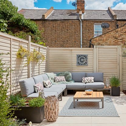 Outdoor seating area with corner sofa in front of cream painted fence