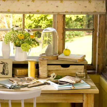 A craft room with a wooden desk facing a window with plenty of natural light