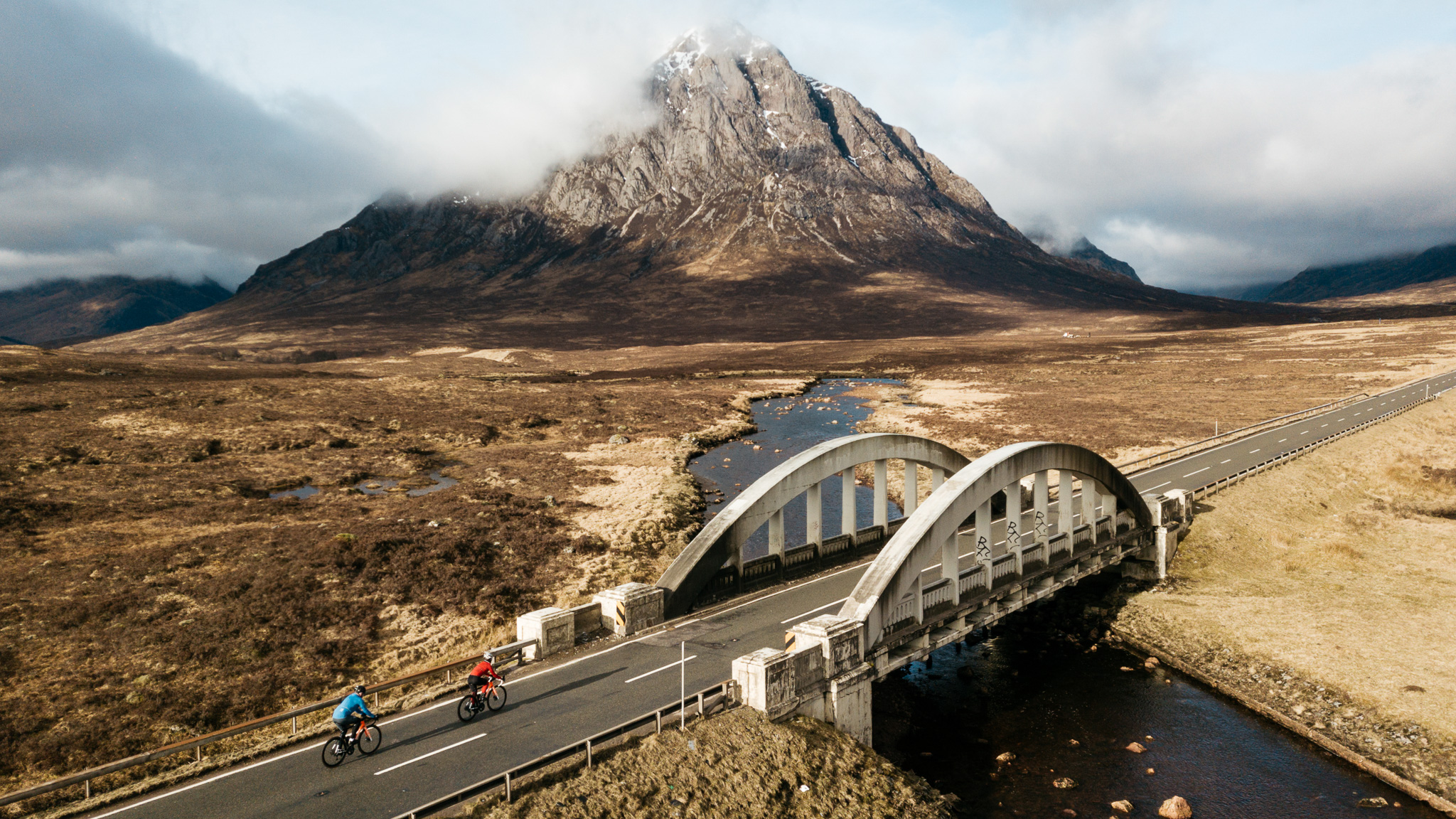 Two cyclists riding over a bridge in Glencoe, Scotland, with Buachaille Etive Mor i background
