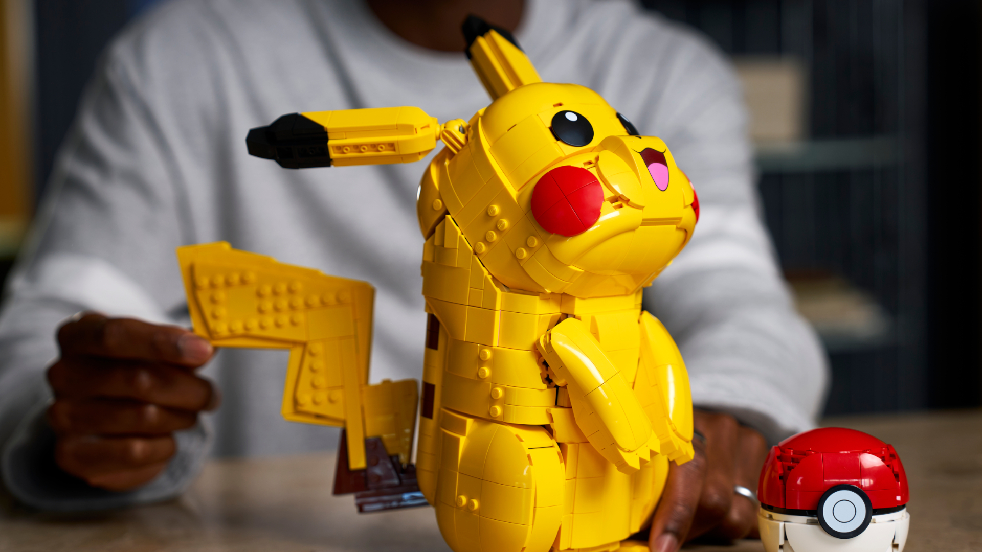 Lego Pikachu looking upward, while a hand moves the tail