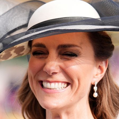 Princess Kate wearing a white hat with a black ribbon and smiling