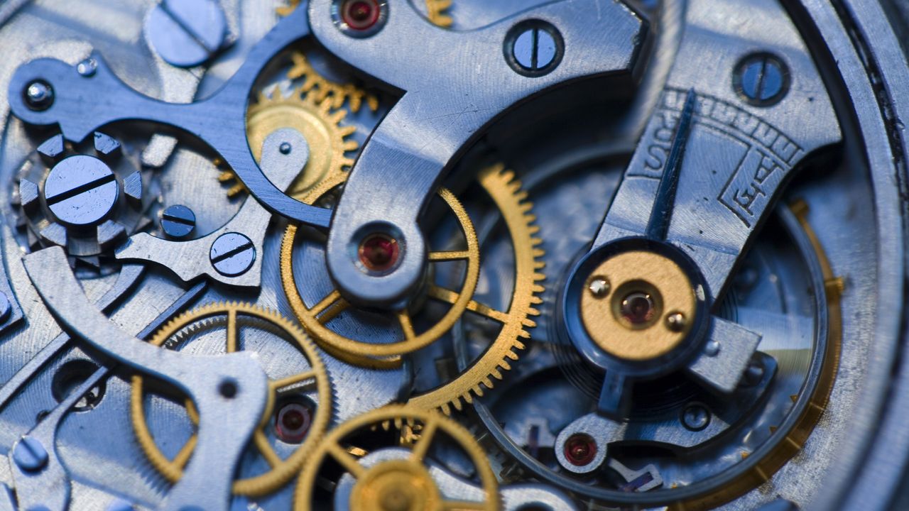 A close up of the movement inside a watch, with a mix of yellow and white coloured metals and some bright red jewels