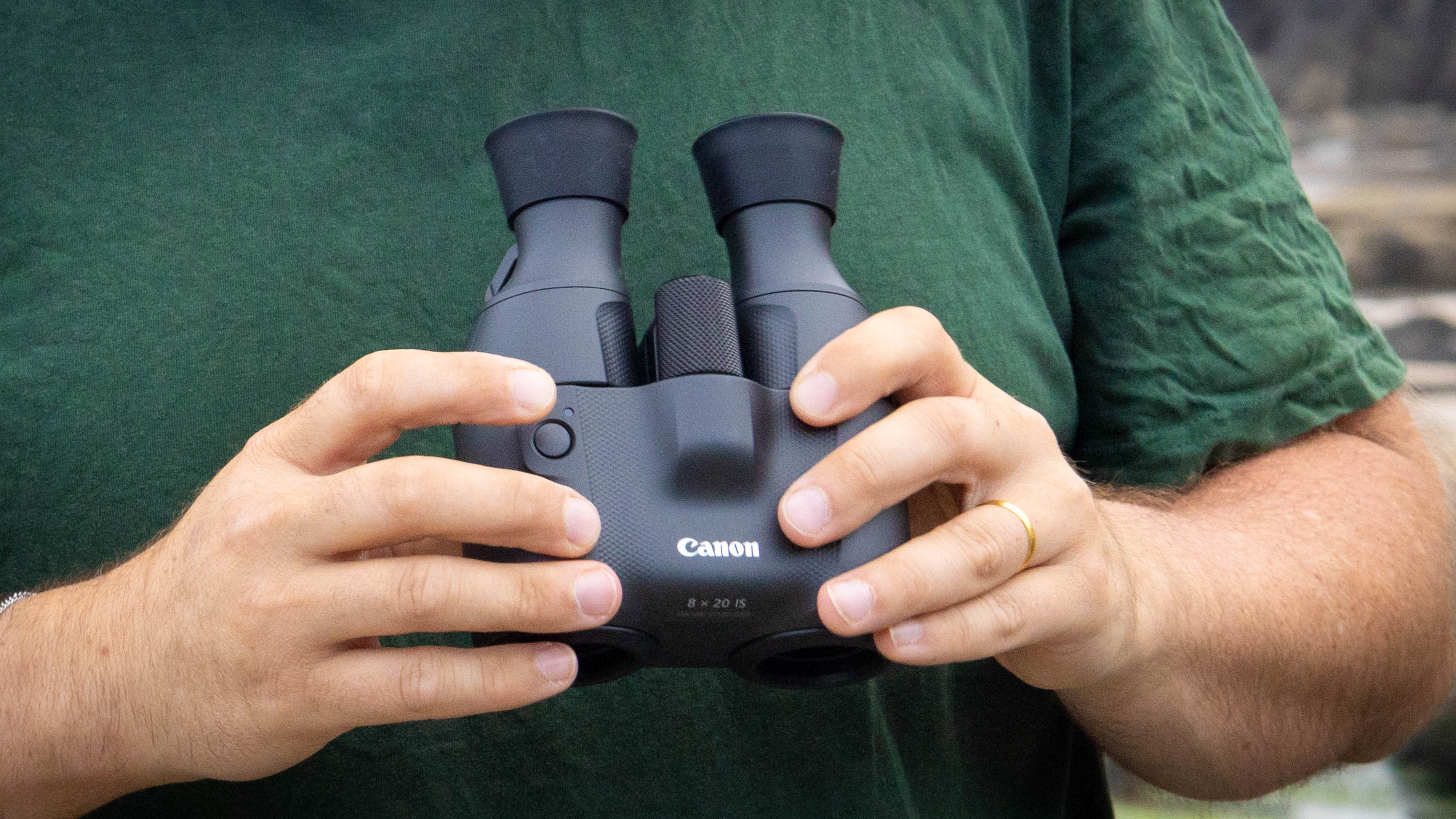 A person holding the Canon 8x20 IS showing the IS button.