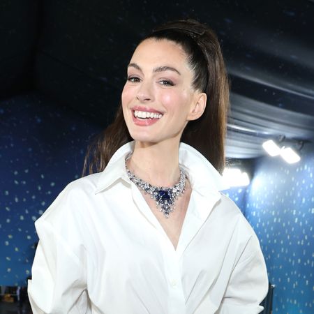 Anne Hathaway attends the Met Gala 2025 wearing a white shirt with a large diamond and sapphire necklace and a scraped back ponytail