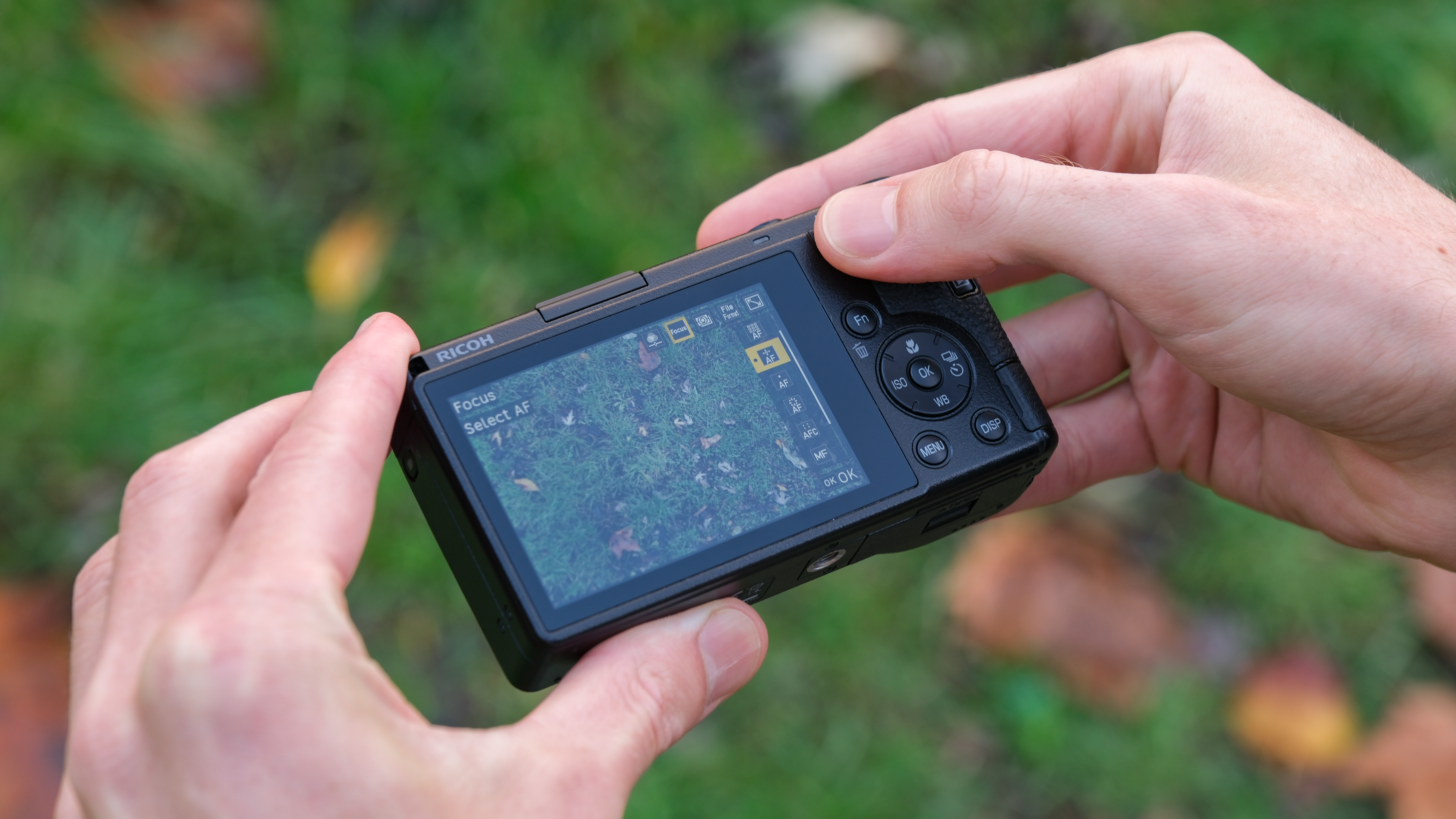 Ricoh GR IV compact camera held in a pair of hands