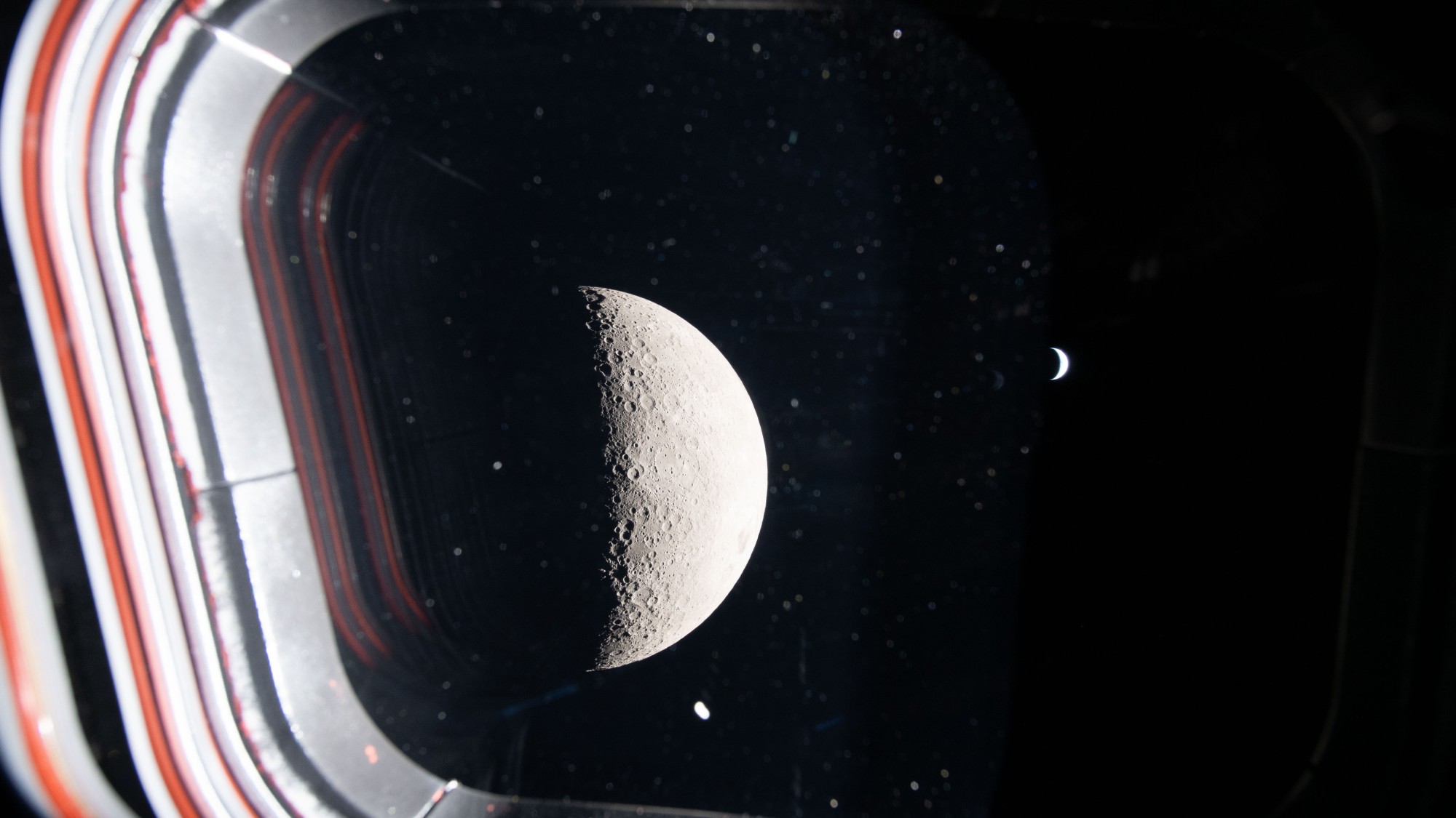 a pockmarked grey orb and a bright crescent seen on a starry background through a window