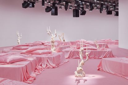 The Acne Studios S/S 2023 show set at Paris’ Palais de Tokyo, with candelabras by Sylvie Macmillan on platforms with pink sheets and pillows on them.