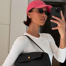 A woman taking a mirror selfie wearing a Ralph Lauren cap and sunglasses with a bob haircut