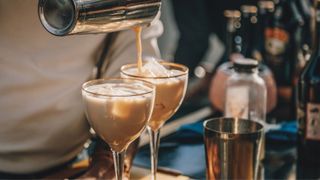 Irish cream being poured into glass through aluminium beaker and mixer