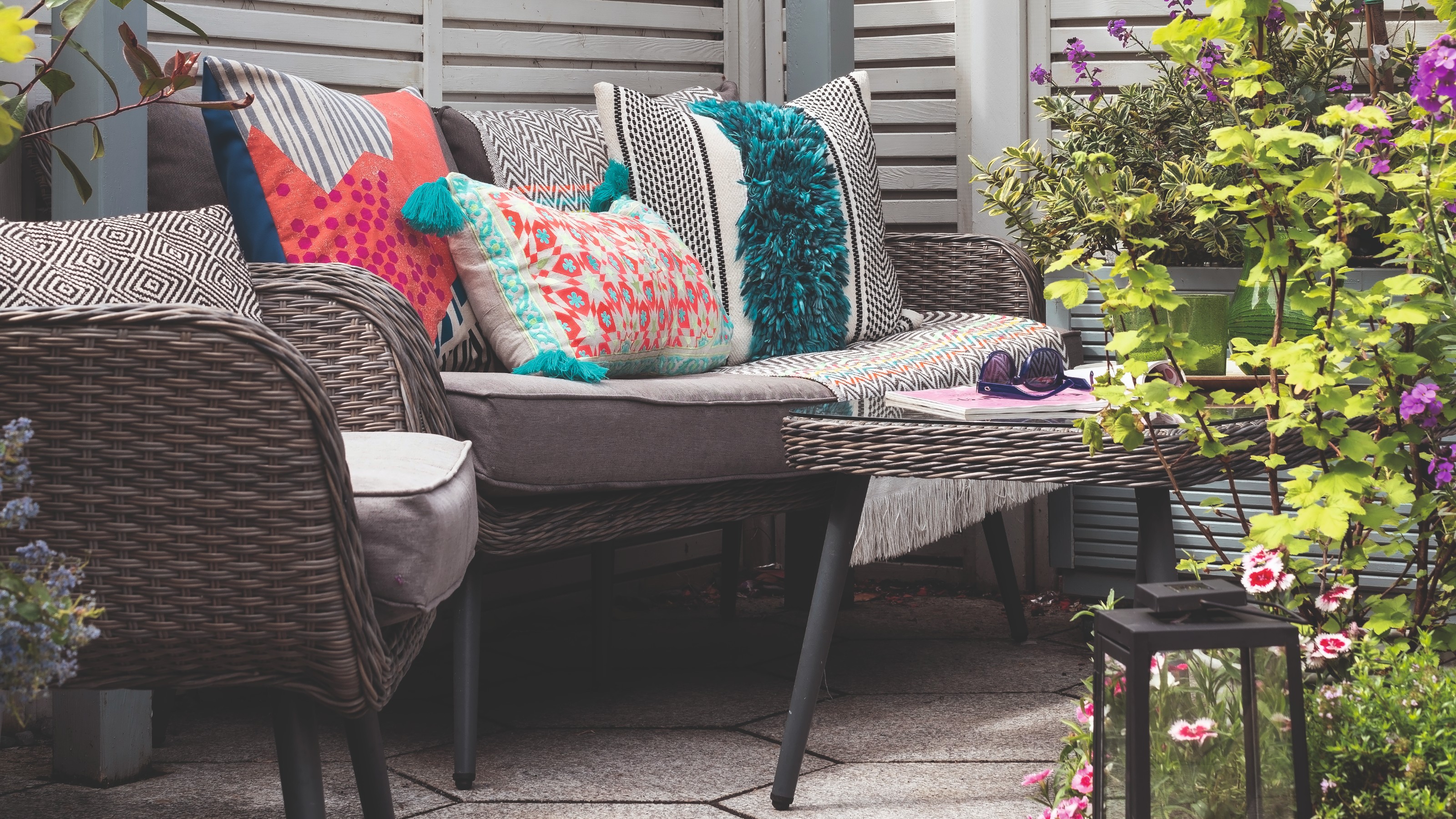 A rattan-effect set of outdoor sofa and chair in grey with grey seat cushions and colourful scatter outdoor cushions