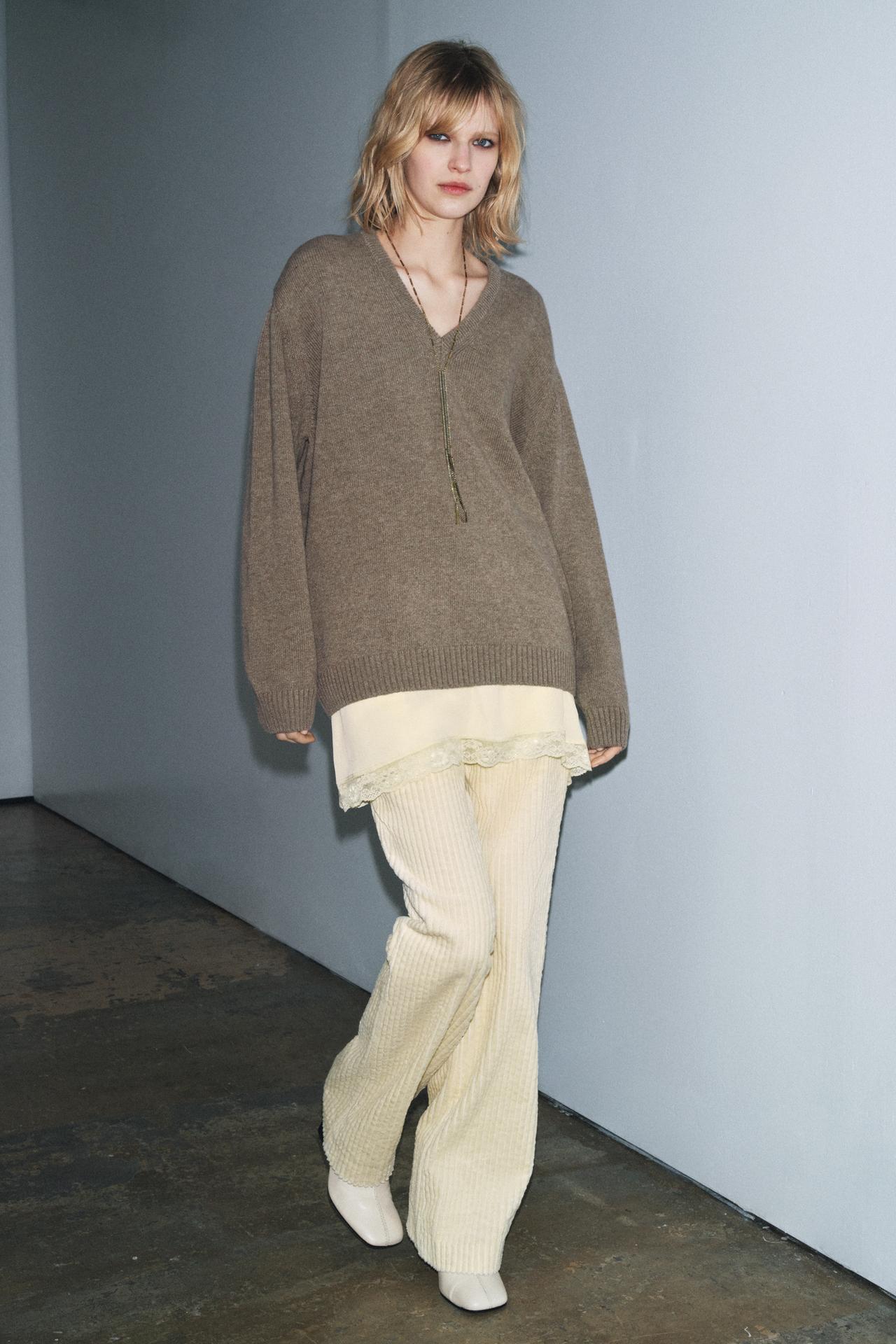 Model wears oversized v-neck sweater layreed over long-line lace camisole, matching trousers, and white square toe boots.