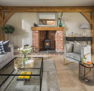 A red brick fireplace with a wood burner in a living room with an armchair and glass coffee table