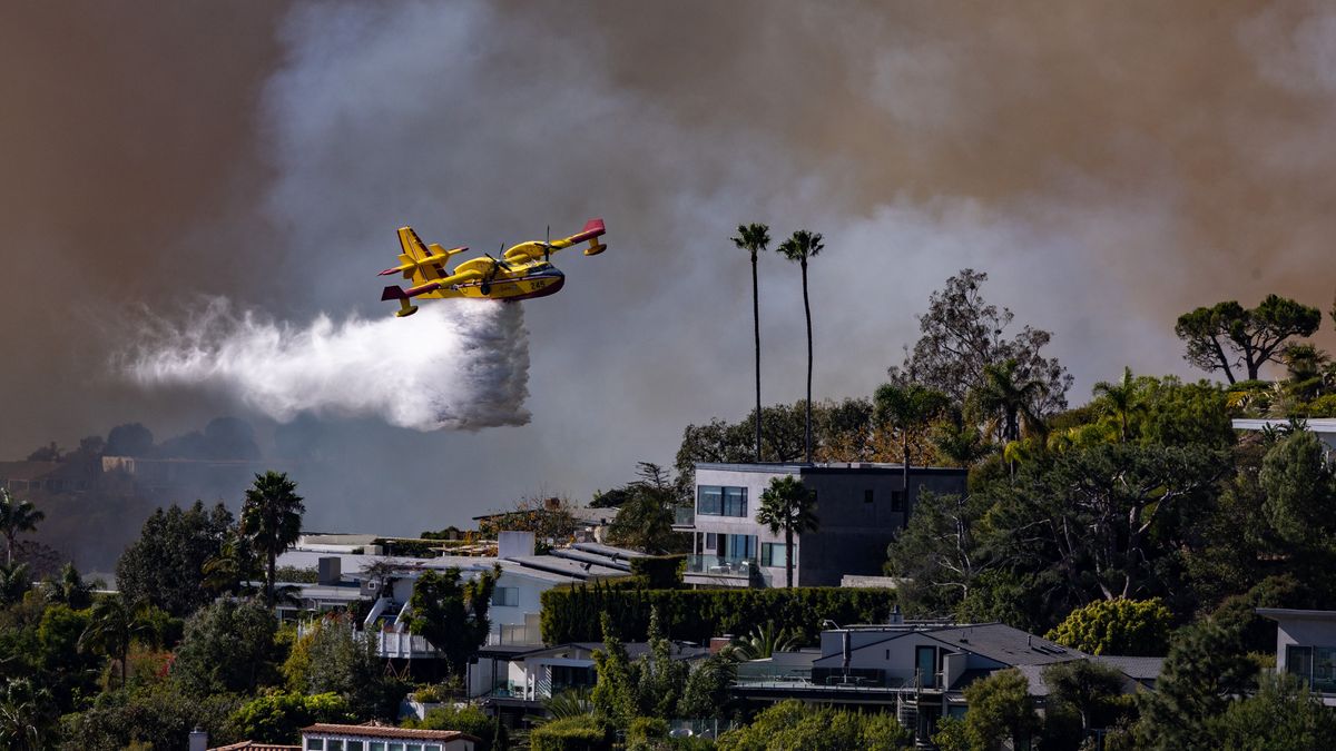 A super scooper airplane drops water on buildings at the Palisades fire