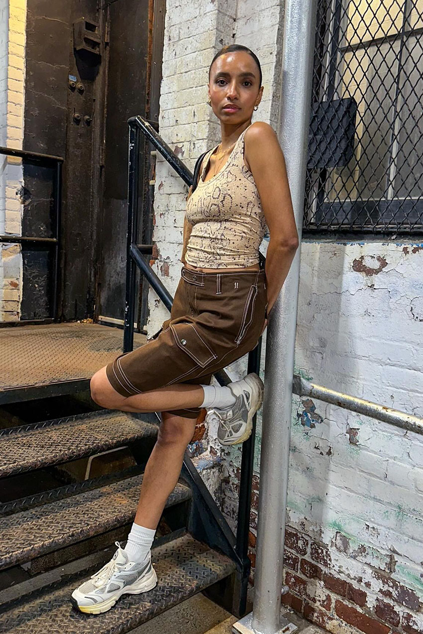 A woman wearing tank top, brown shorts, and white chunky sneakers.