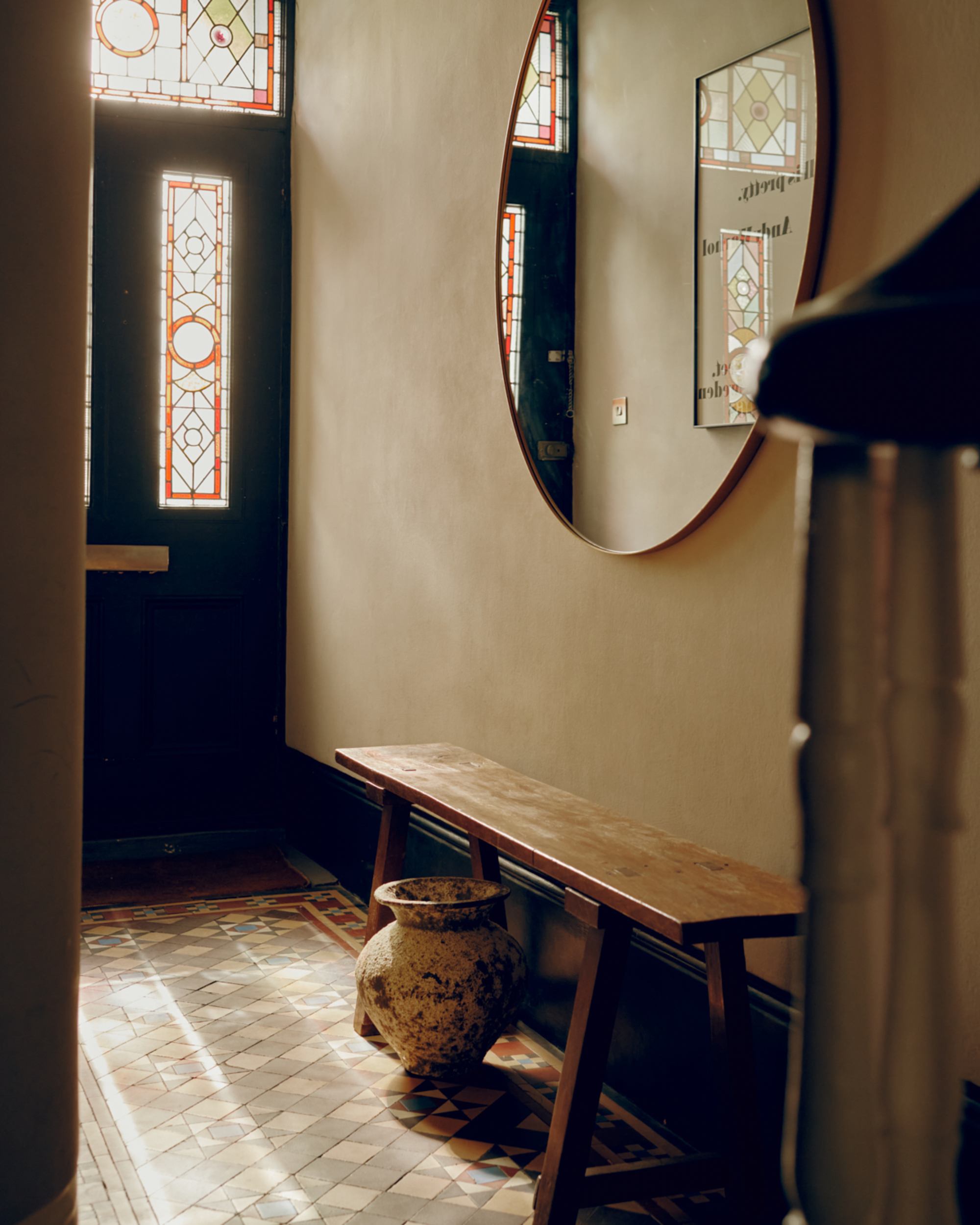 The entry hallway with original tiled floor and a wooden bench with a large mirror hanging above