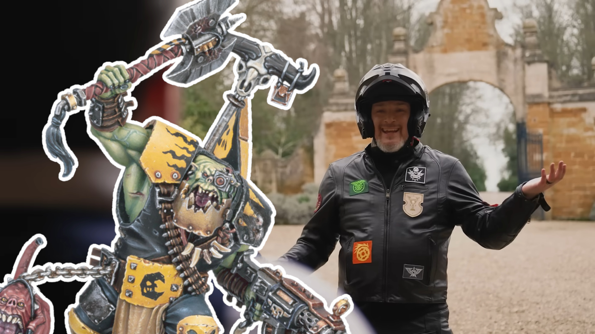 Adam Troke in a biker jacket and helmet smiles, with an Ork miniature in front of him outlined in white