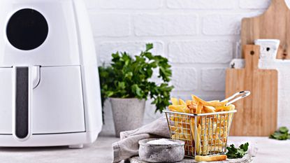 A white air fryer in a white kitchen besides some fresh fries 