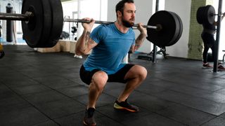 Man performing barbell back squat in gym