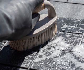 Person using a bristled cleaning brush to clean a patio