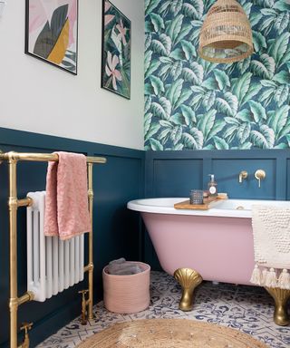 Playful bathroom with jungle wall paper, teal paneling, and pink freestanding bath