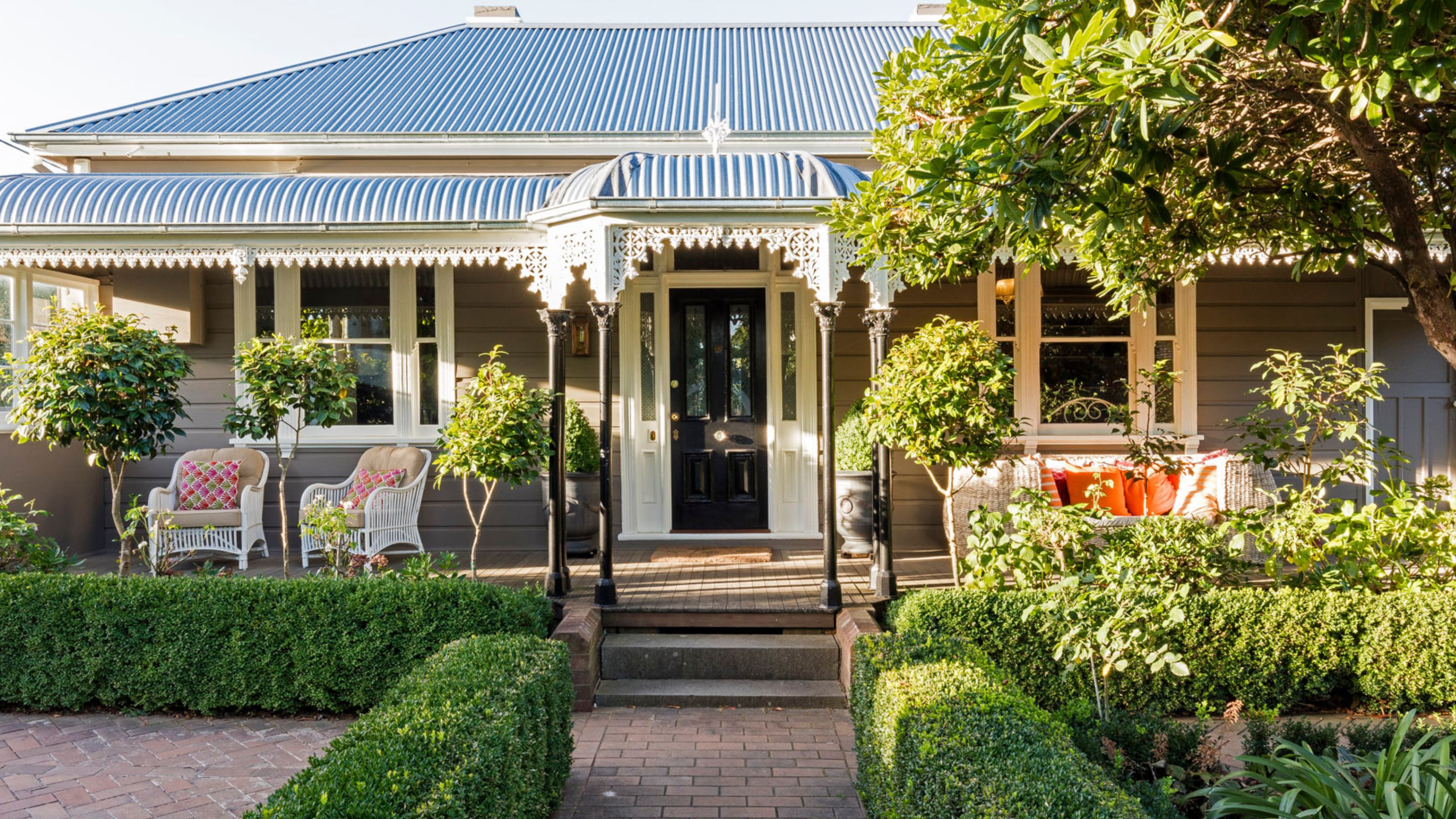 The facade of a home with lots of plants scattered around as well as a black traditional style door. There is patio furniture on the left and right side of the home. 