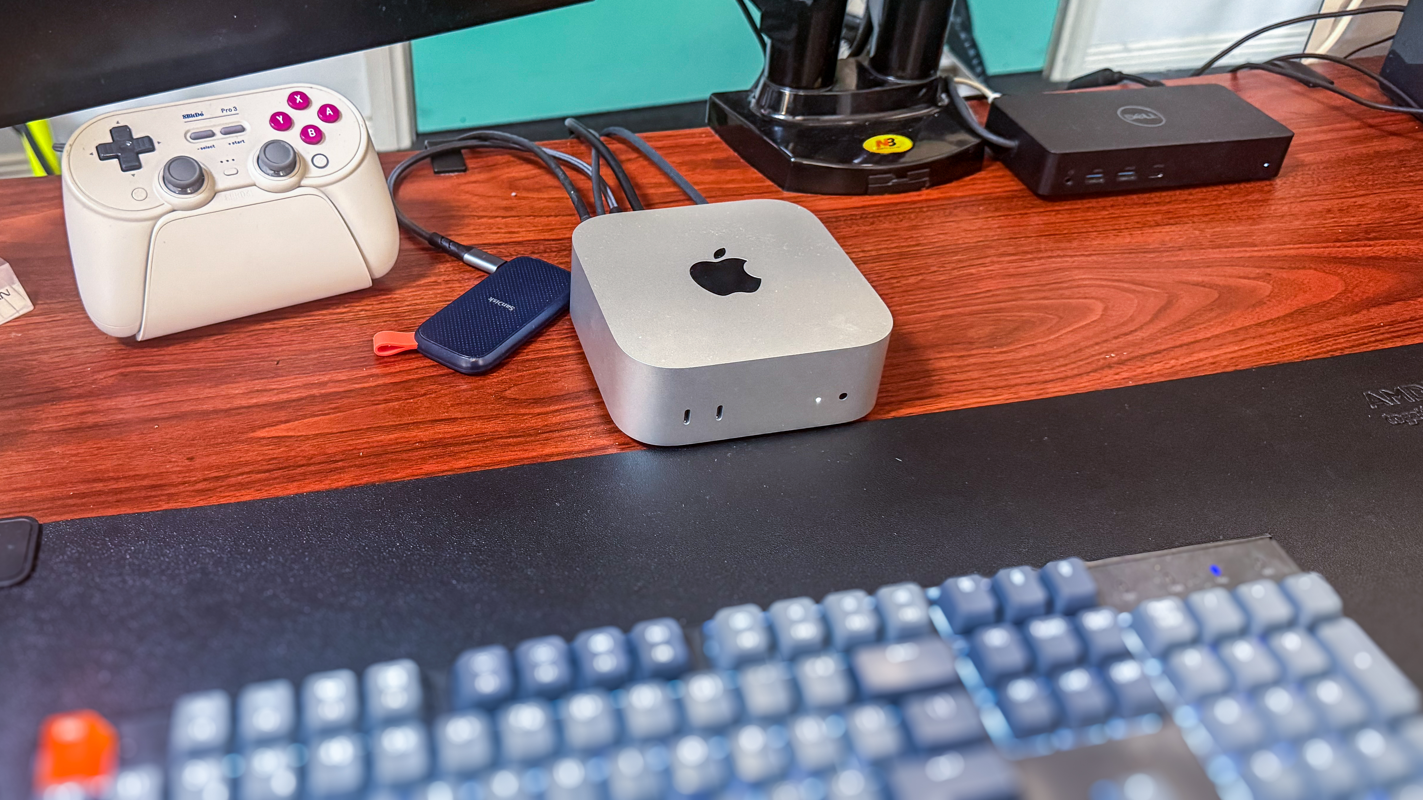 An Apple Mac mini M4 on a desk with a dock, controller, portable SSD and keyboard