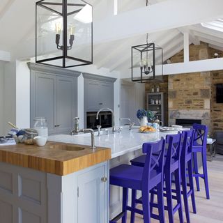 white gloss island with wooden end, bright purple stool and lantern style pendants