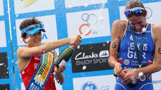 Triathletes Barbara Riveros Diaz and Helen Jenkins celebrate by spraying champagne on a podium