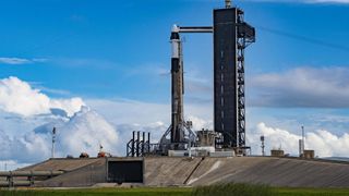 a rocket stands at a launchpad in front of a blue sky with majestic clouds