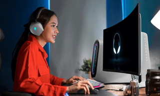 A woman wearing an Alienware headset using an Alienware keyboard, gaming PC and monitor from Dell.