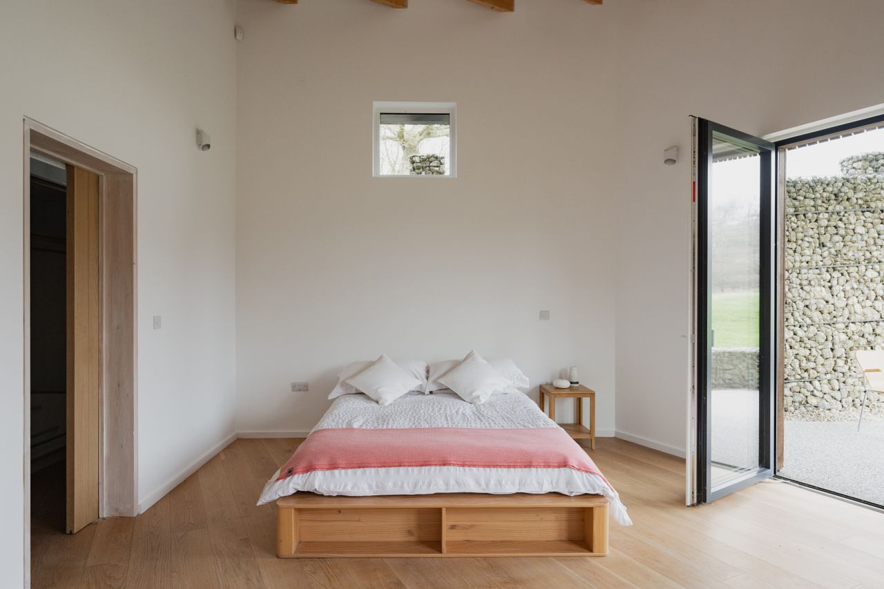 A low bed next to bifold doors with an en suite bathroom
