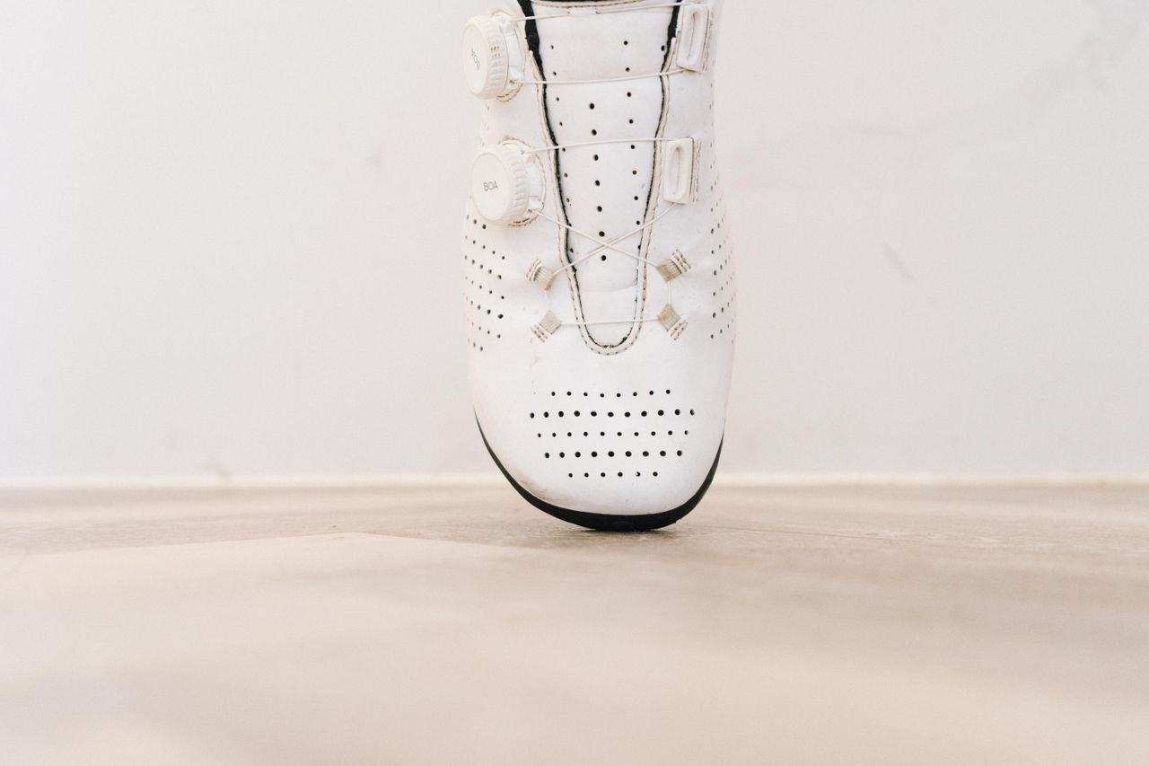 A close up of a white cycling shoe with a black socked foot in it