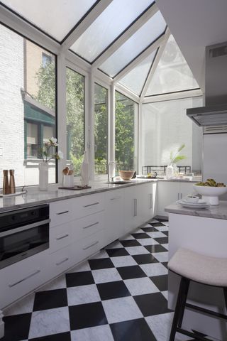 Chequered floor tiles in sunroom come kitchen with white cabinetry and bar stools
