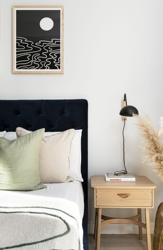 white bathroom with black bed, black and white artwork, blond wood side table, wall light, pastel bedding