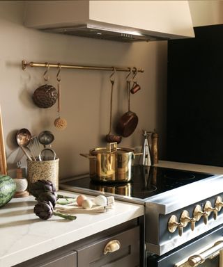 A stovetop with a gold pot and utensils hanging behind.