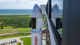 a white space capsule sits atop a rocket on the launch pad, with greenery and the ocean in the background