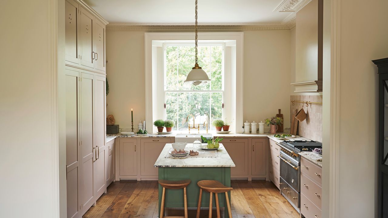 small u-shaped kitchen with cream walls and warm wood floor pink cabinetry and green island all with marble worktops