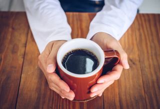 Types of headaches: Someone hands holding a mug of black coffee before drinking