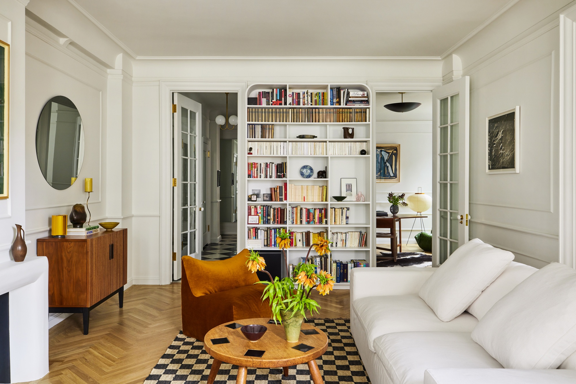 a white apartment living room with neutral furniture a bookcase and views to another two rooms
