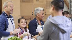 A young girl helps serve food at a soup kitchen.