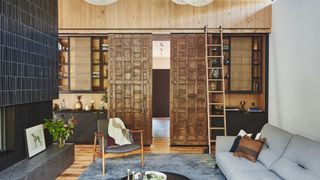 Rustic carved wooden sliding doors between shelving units, string pendant lights, grey sofa and armchair.