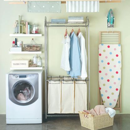 A laundry room with a washing machine, hanging laundry and a polka dot ironing board