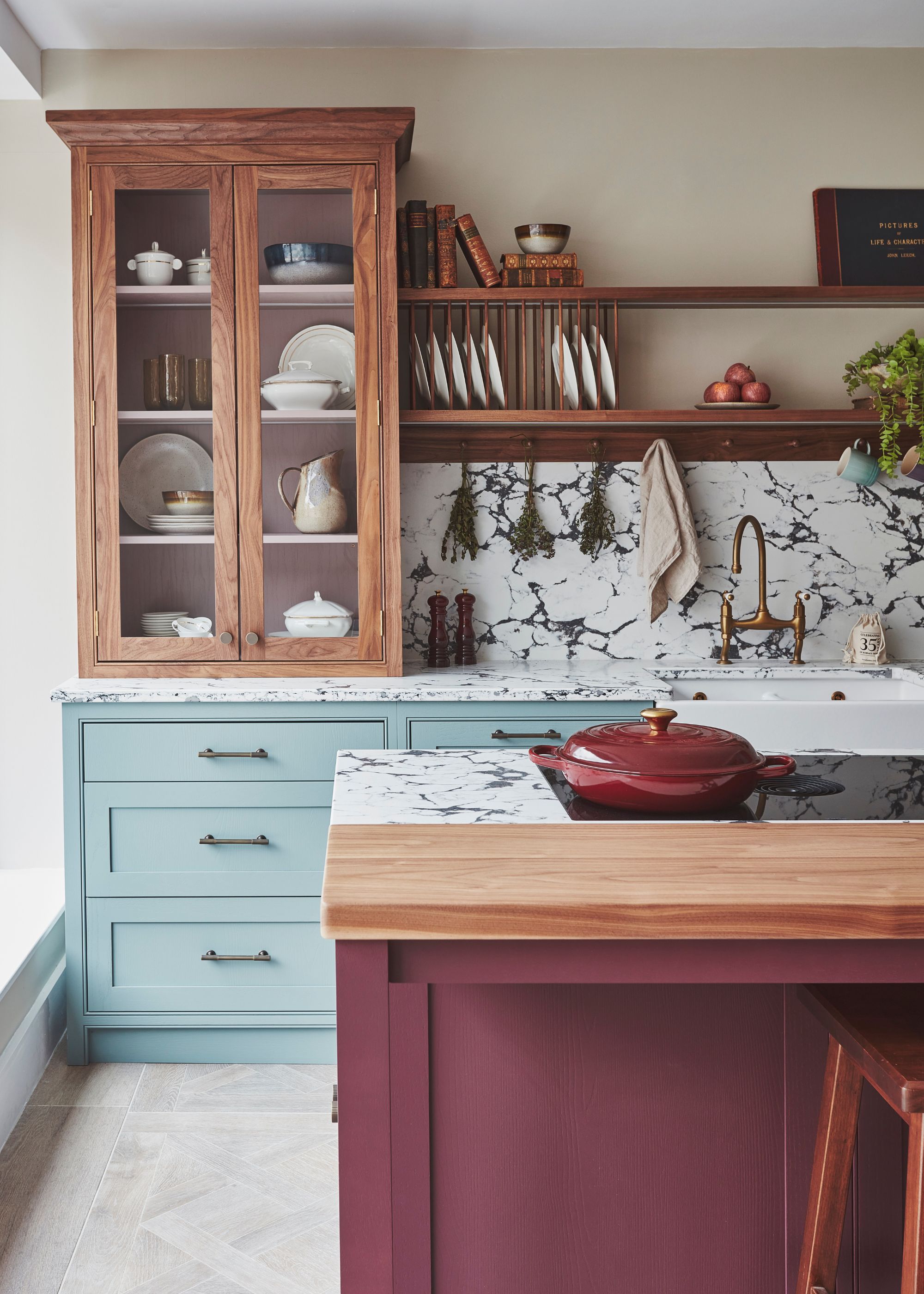A kitchen with glass fronted cabinets with plates and dishes. As well as open shelving and an area to set plates. There is also a view of the kitchen island and hob that has a pan with a lid on top of it.