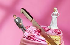Wedding cake with models of bride and groom on either side of knife embedded in cake 