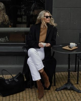 woman in white jeans, black coat and brown suede boots