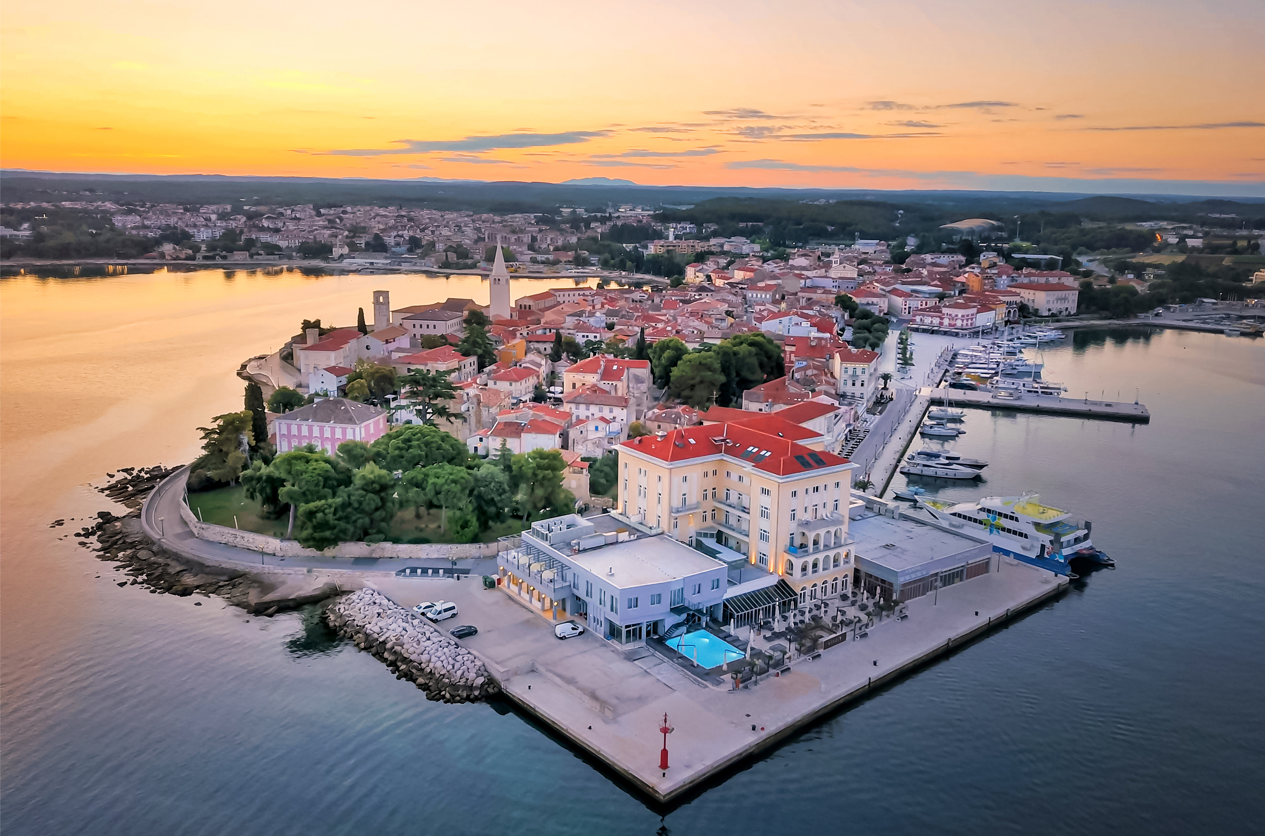 Birds eye view of Poreč at sunset, a town jutting out into water with cream buildings with red rooves