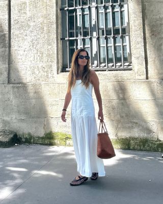 Woman wears a white drop waist dress with Alaia mesh flats.